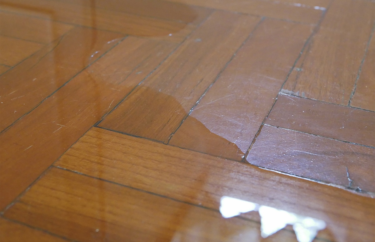 Superficie de parquet con manchas y marcas de humedad visibles, mostrando zonas oscurecidas y levantadas por la absorción de agua