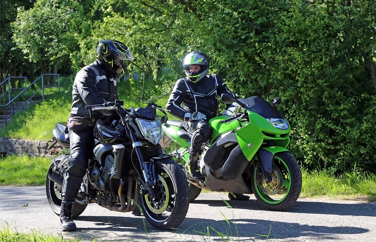 2 motoristas sobre su moto parados en una carretera hablando