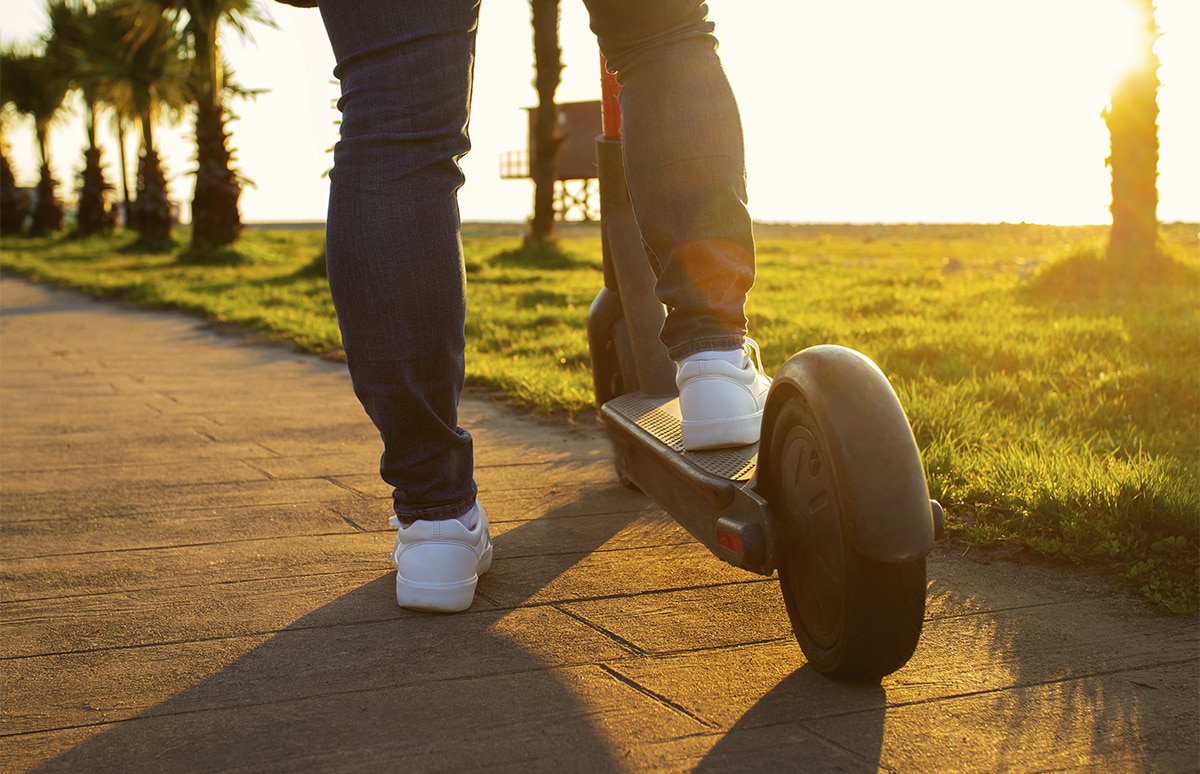 Joven en un paseo con un pie sobre su patinete eléctrico