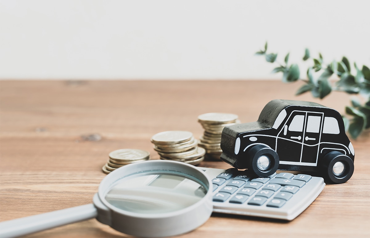 Coche en miniatura sobre una calculadora, al lado de monedas y una lupa