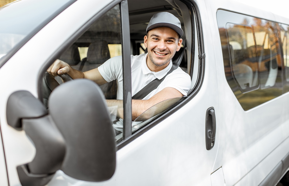 Transportista sonriente al volante de un vehículo mixto adaptable