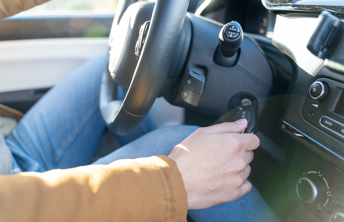 Primer plano del lateral derecho de un volante con una mano girando la llave que hay en el contacto