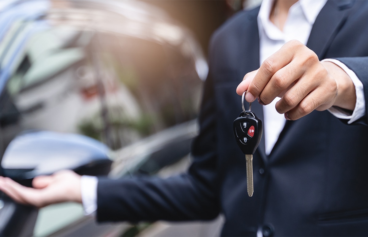 Vendedor entregando las llaves del coche que hay a su lado