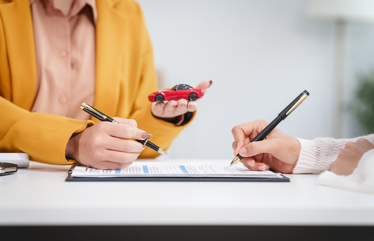 Dos mujeres firmando un contrato, una de ellas con un coche en miniatura rojo en su mano izquierda