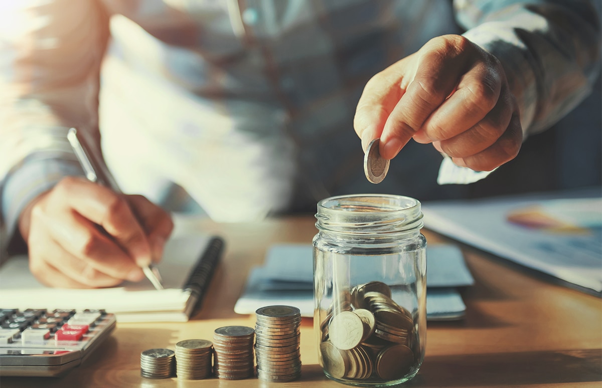 Hombre realizando cuentas y metiendo dinero en un tarro de cristal