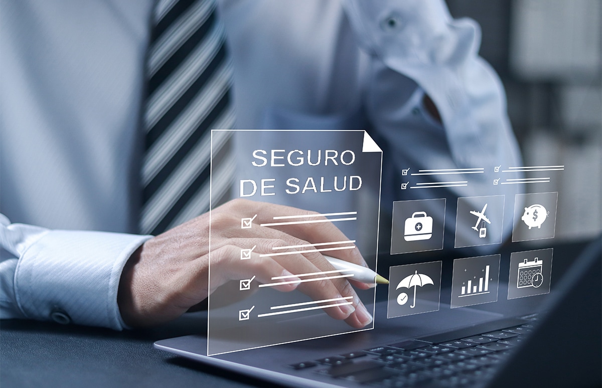 Mano interactuando con un panel digital sobre un seguro de salud junto a un portátil.