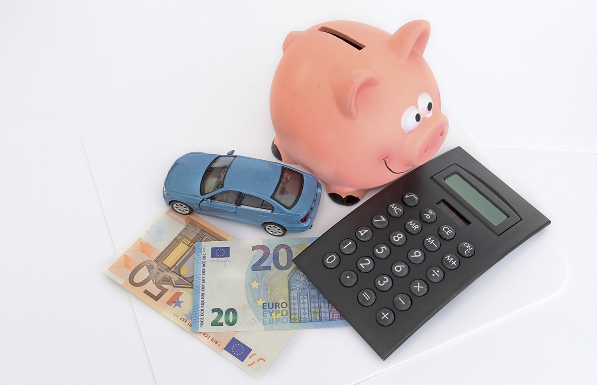 Hucha, coche en miniatura, billetes y calculadora representando gestión y ahorro financiero