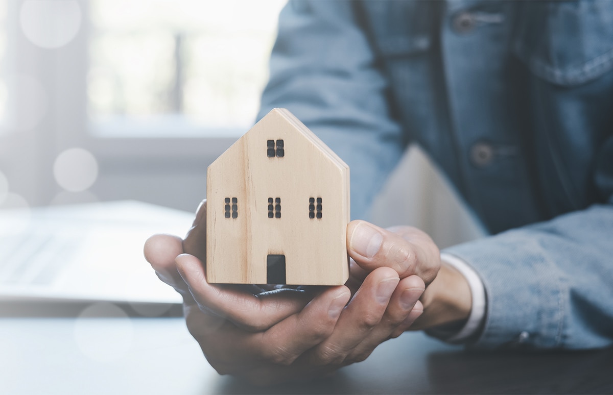 Maqueta de una casa de madera sobre las manos de un hombre