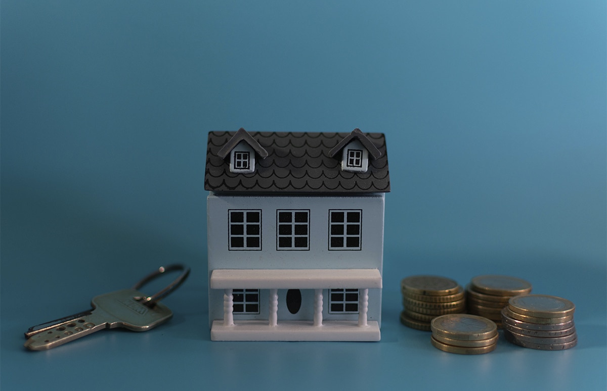 Maqueta de una vivienda con las llaves a un lado y monedas al otro