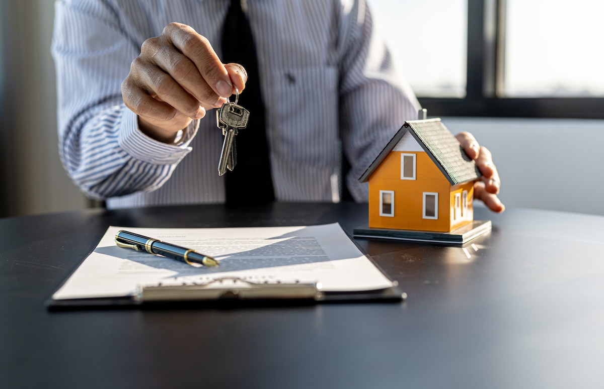 Entrega simbólica de llaves junto a la firma de documentación inmobiliaria, representando la contratación o protección de una vivienda mediante un seguro de hogar