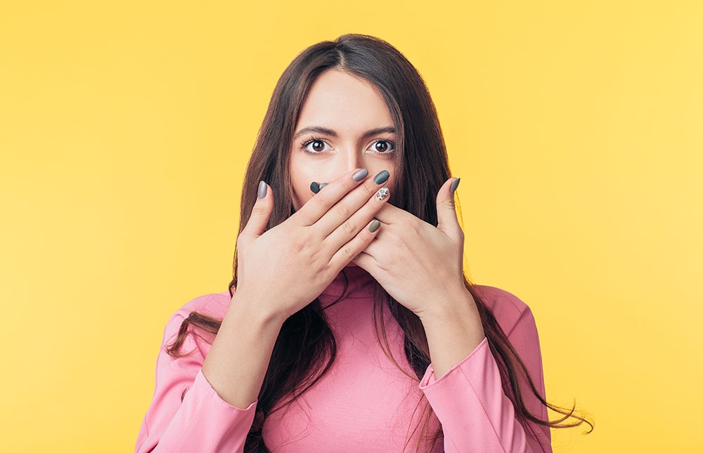 Surprised excited woman covering her mouth with hands isolated on yellow background