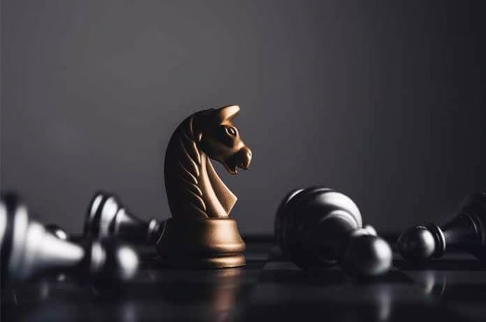 Caballo de ajedrez dorado junto a piezas plateadas vencidas