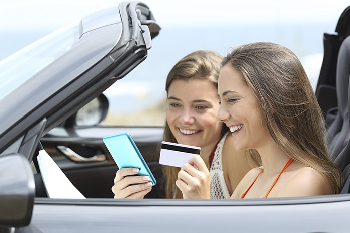 2 chicas jóvenes dentro de un descapotable mirando el móvil con una tarjeta bancaria en la mano