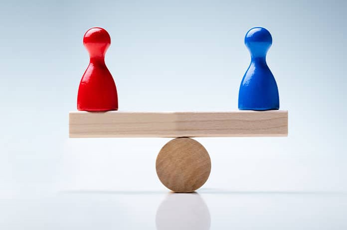 Dos figuras de colores rojo y azul colocadas en equilibrio sobre una balanza de madera, simbolizando comparación o igualdad