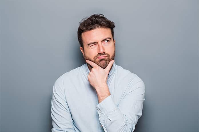 Persona pensativa con la mano en el mentón frente a un fondo gris, reflejando duda o reflexión