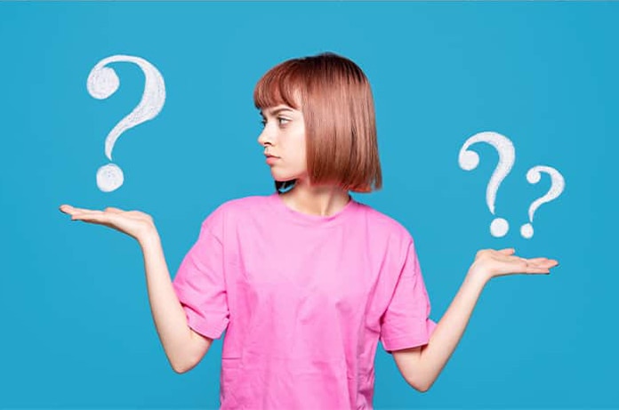 Persona con una camiseta rosa levantando las manos mientras aparecen signos de interrogación a su alrededor sobre un fondo azul