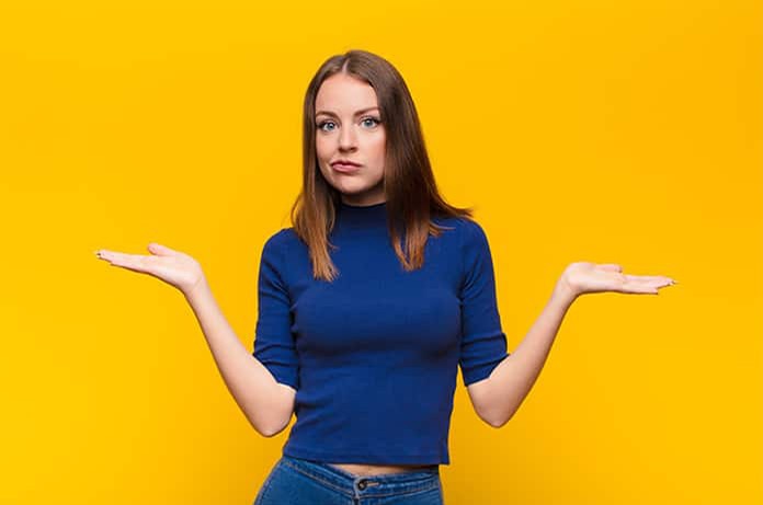 Persona con los brazos abiertos hacia los lados sobre un fondo amarillo, transmitiendo comparación o duda