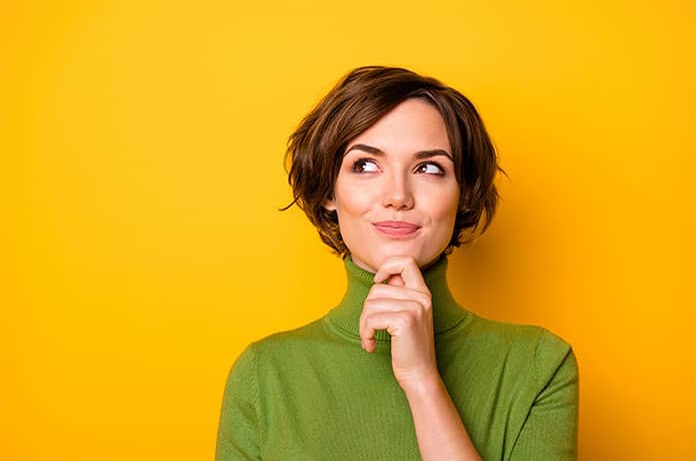 Persona con gesto pensativo y la mano en el mentón frente a un fondo amarillo brillante