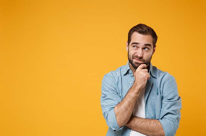 Hombre en actitud pensativa, con la mano en el mentón frente a un fondo amarillo intenso
