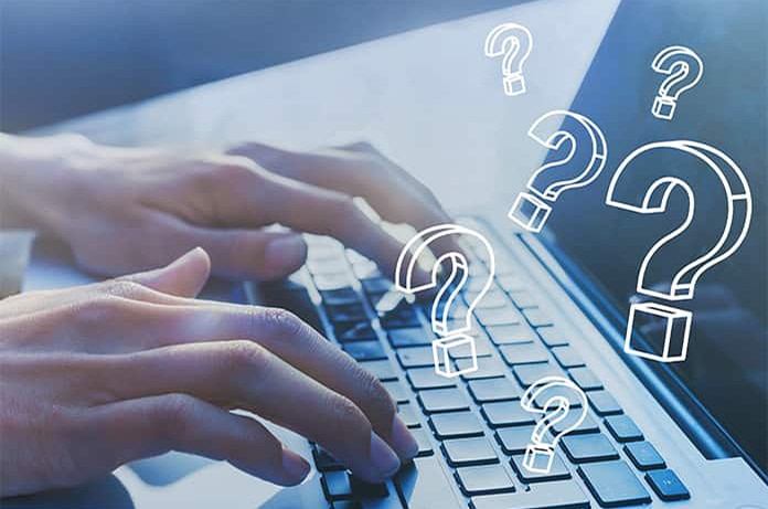 Manos tecleando en un ordenador portátil con varios signos de interrogación flotando sobre la escena