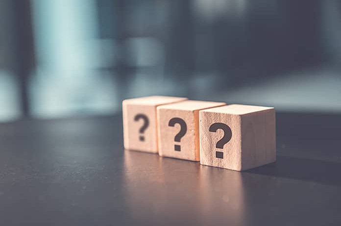 res cubos de madera alineados sobre una superficie oscura, cada uno con un signo de interrogación impreso, simbolizando dudas o preguntas frecuentes