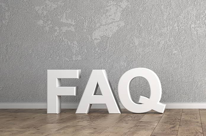 Grandes letras blancas “FAQ” colocadas sobre un suelo de madera frente a una pared gris