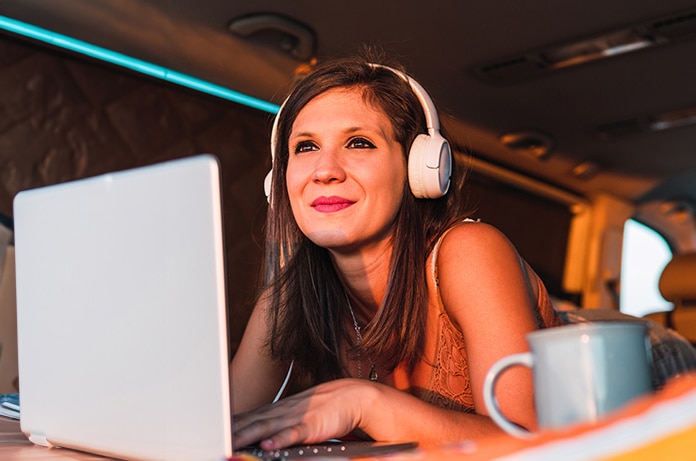Mujer joven utilizando un portátil dentro de una furgoneta acondicionada, usando auriculares mientras mira el atardecer