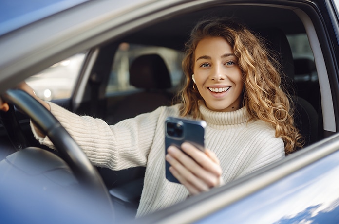 Chica sonriente al volante de un coche parado mirando su móvil