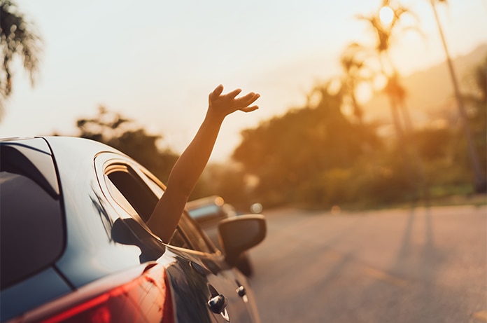 Brazo extendido fuera de la ventanilla de un vehículo mientras circula por una carretera al atardecer