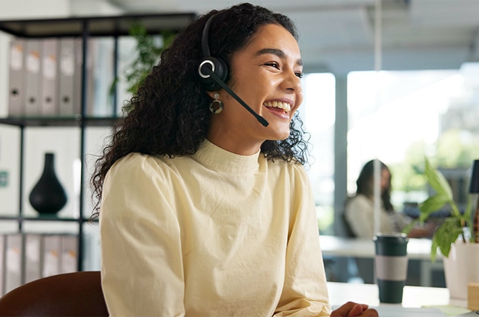 Persona con auriculares participando en una conversación dentro de un espacio de trabajo con documentación y material de oficina al fondo