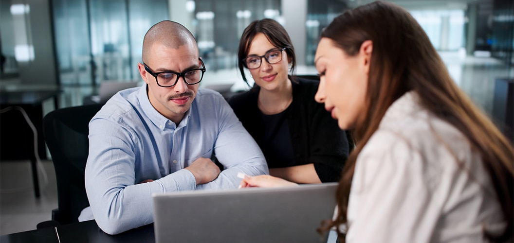 Grupo reunido en una sala de oficina, revisando información en un ordenador portátil durante una consulta presencial