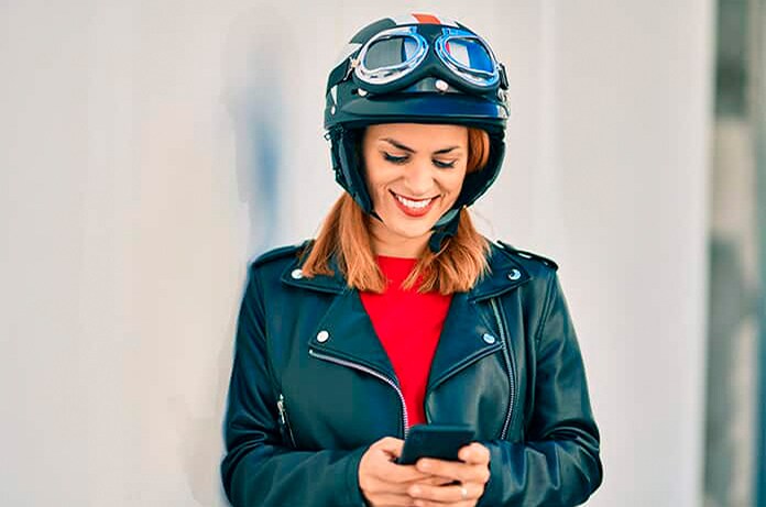 Figura con chaqueta y casco retro consultando un teléfono móvil mientras está apoyada contra una pared