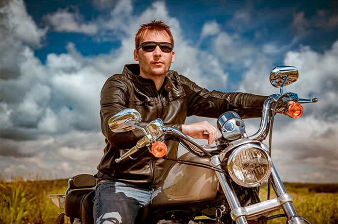 Persona sentada sobre una motocicleta en un camino abierto, rodeada de un paisaje natural con nubes y horizonte despejado