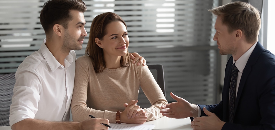 Dos personas sentadas juntas frente a un profesional en una mesa de trabajo mientras revisan documentación