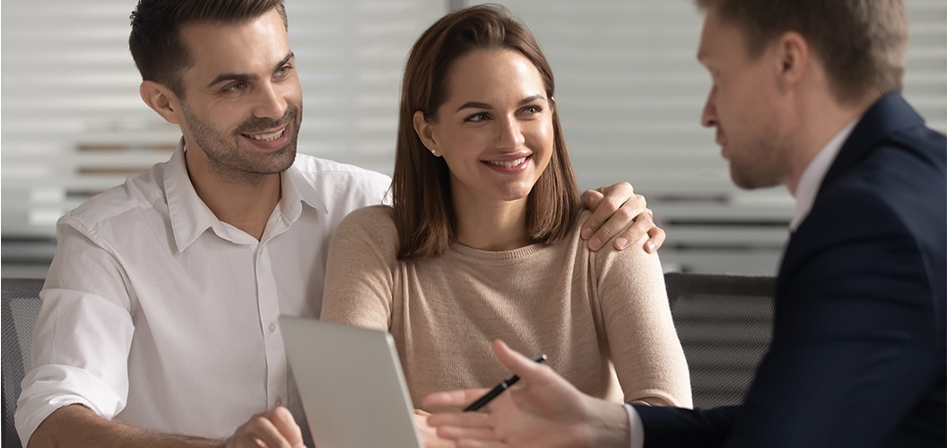 Tres personas reunidas en una mesa mientras dialogan con un profesional que sostiene un bolígrafo y unos documentos