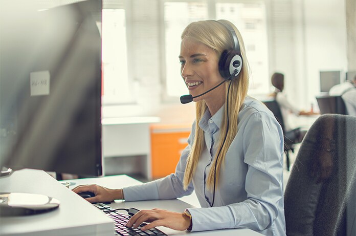 Figura utilizando auriculares con micrófono mientras trabaja frente a un ordenador en un entorno de oficina iluminado
