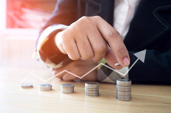 Mano apilando monedas en pequeñas columnas mientras una flecha ascendente representa crecimiento financiero