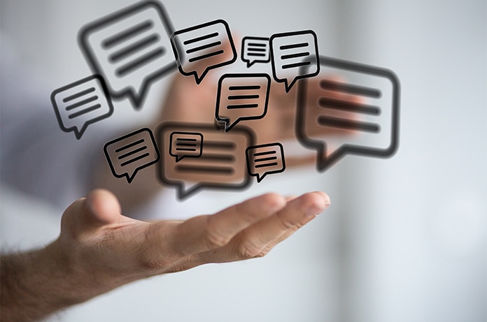 Mano extendida en primer plano sosteniendo iconos gráficos de bocadillos de diálogo superpuestos, que representan intercambio de opiniones o comunicación