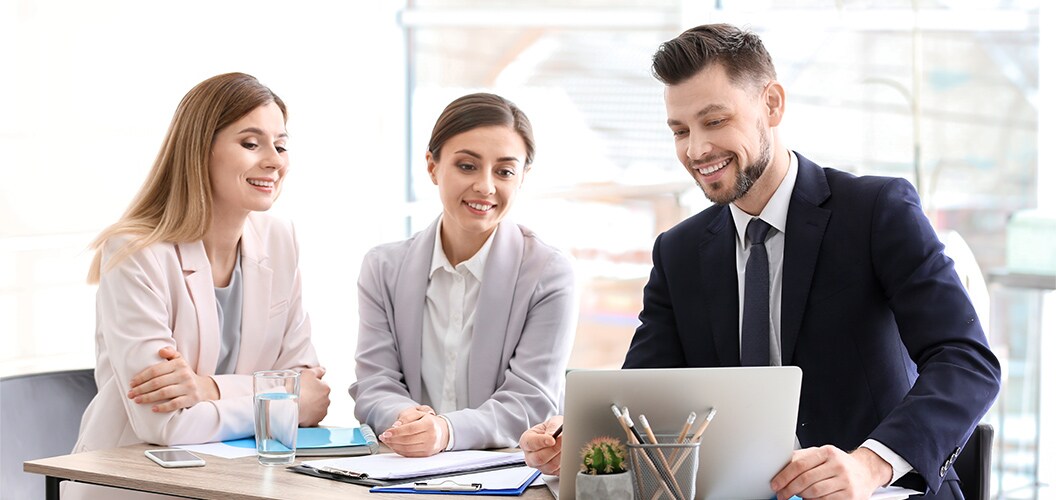 Varias personas reunidas en una mesa de trabajo mientras revisan documentos y un ordenador portátil en un entorno de oficina iluminado