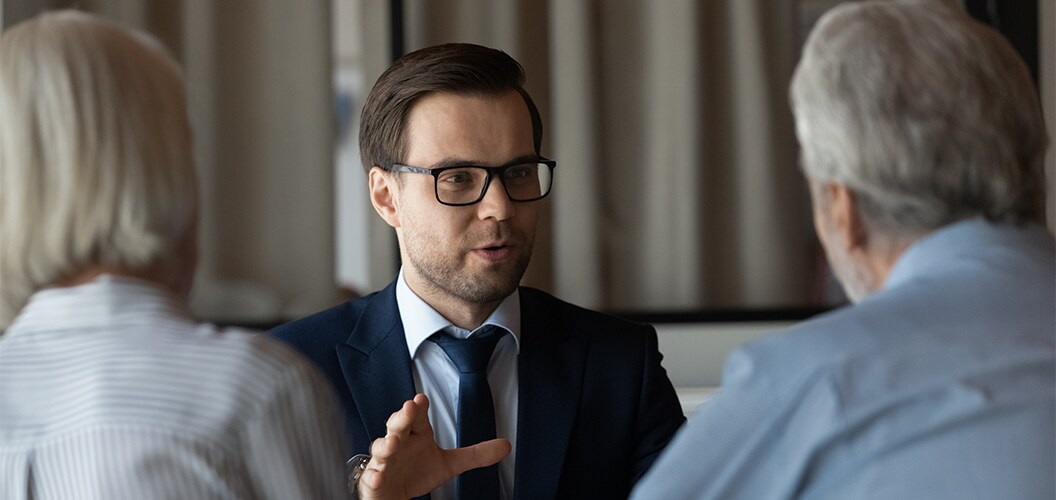 Dos personas sentadas frente a un profesional durante una conversación en un espacio interior con cortinas