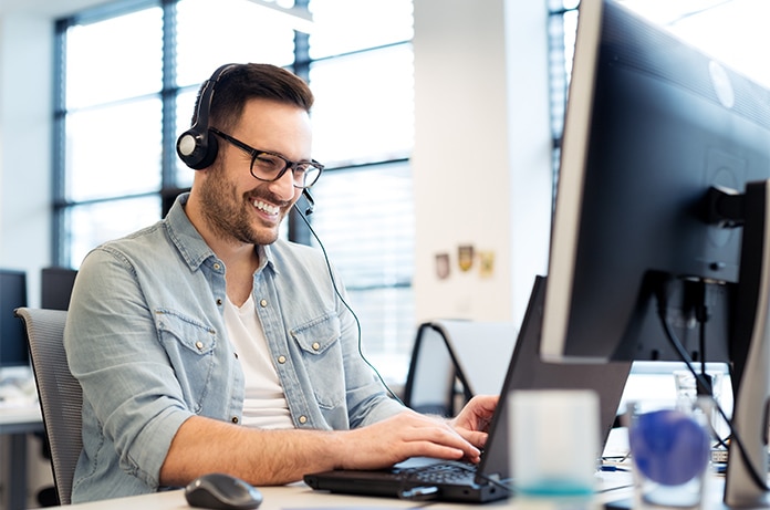 Figura usando auriculares mientras trabaja con un ordenador portátil en un entorno de oficina iluminado por luz natural