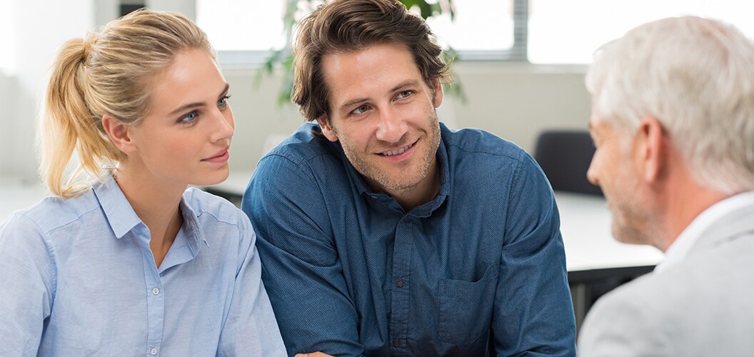 Dos personas dialogando con un profesional en un entorno interior luminoso, sentados alrededor de una mesa de trabajo