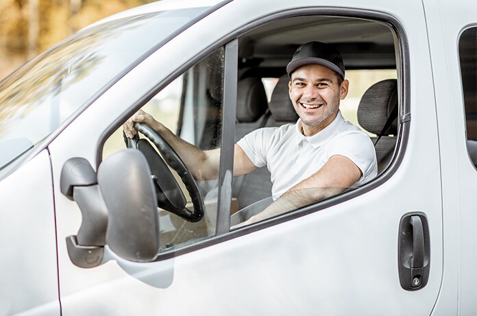 Persona sentada en el asiento del conductor de una furgoneta blanca, sujetando el volante mientras mira hacia el exterior