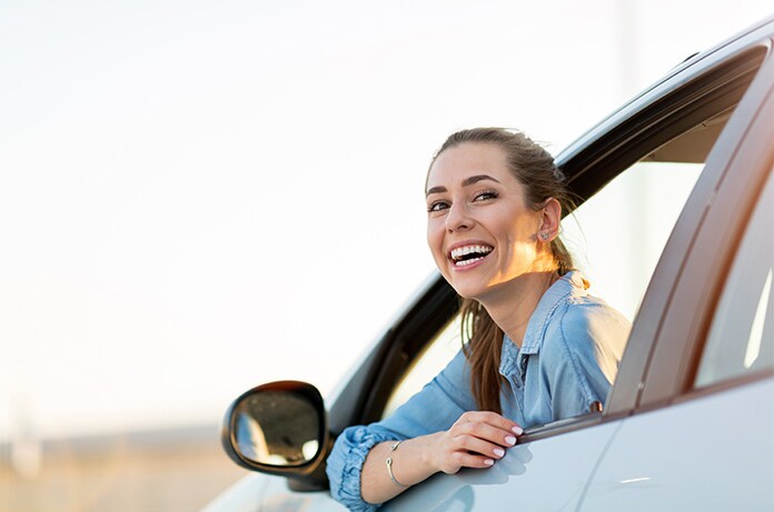 Figura asomada por la ventanilla de un vehículo, apoyando los brazos en el marco de la puerta al atardecer