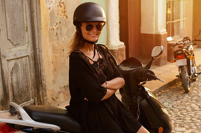 Figura sentada sobre un ciclomotor en una calle adoquinada junto a una fachada envejecida, iluminada por luz cálida