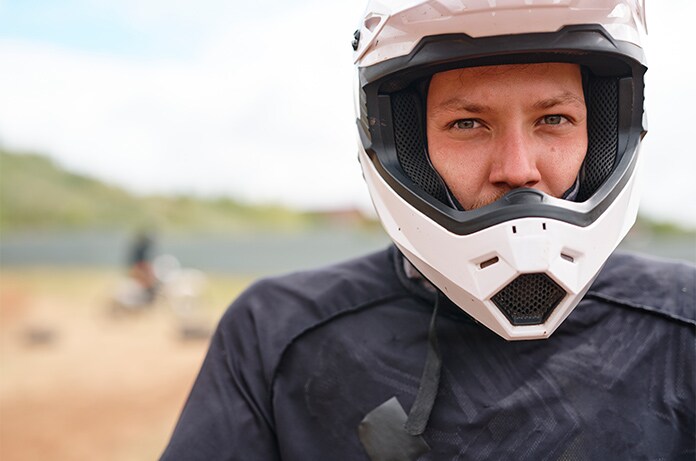 Figura con casco integral y equipación de protección en un entorno de terreno arenoso, con motocicletas desenfocadas al fondo