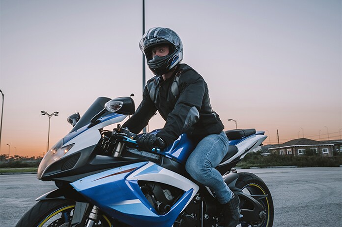 Figura conduciendo una motocicleta deportiva azul en un espacio amplio al atardecer