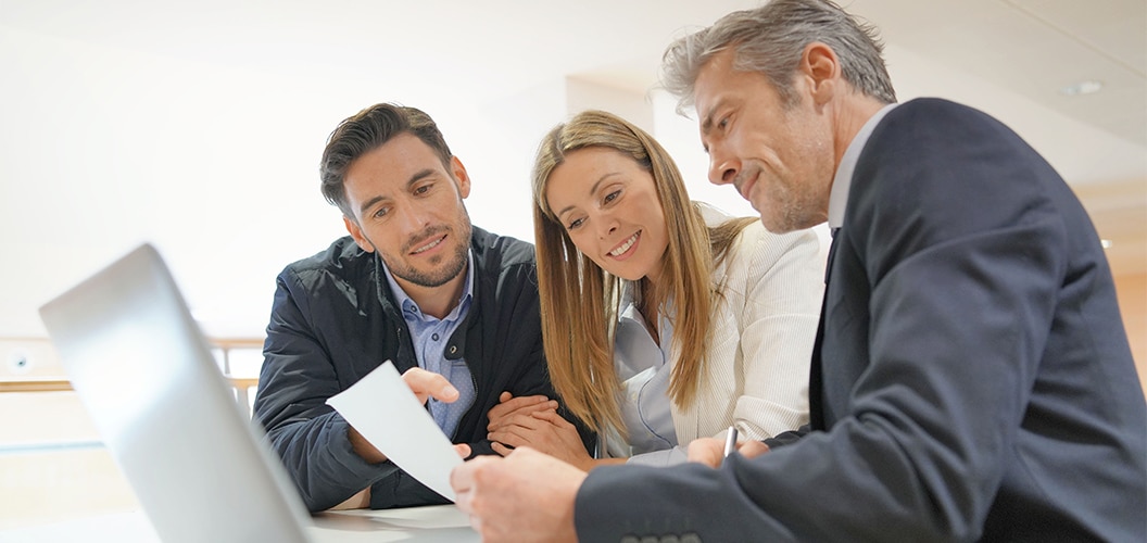 Grupo conversando con un profesional en una mesa de trabajo, mientras revisan documentos en un entorno interior luminoso