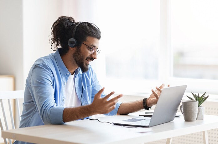 Persona utilizando auriculares mientras gesticula frente a un ordenador portátil durante una videollamada en un espacio luminoso
