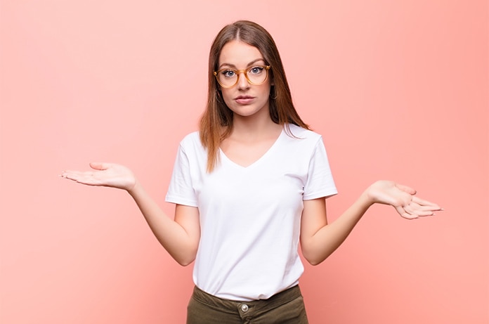 Persona de pie frente a un fondo liso de color coral, con los brazos extendidos y las palmas hacia arriba, adoptando una postura de comparación o elección entre dos opciones
